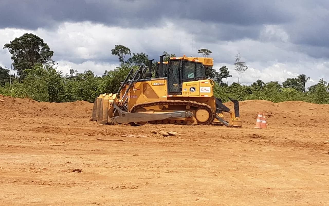 Trator de esteira da FX Minas em área de decapeamento na mineração, com solo vermelho exposto e mata ao fundo